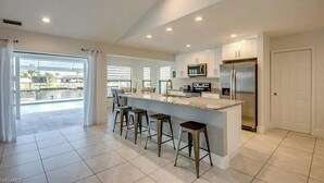 Een moderne keuken met een groot eiland, barkrukken en uitzicht op een zwembad.