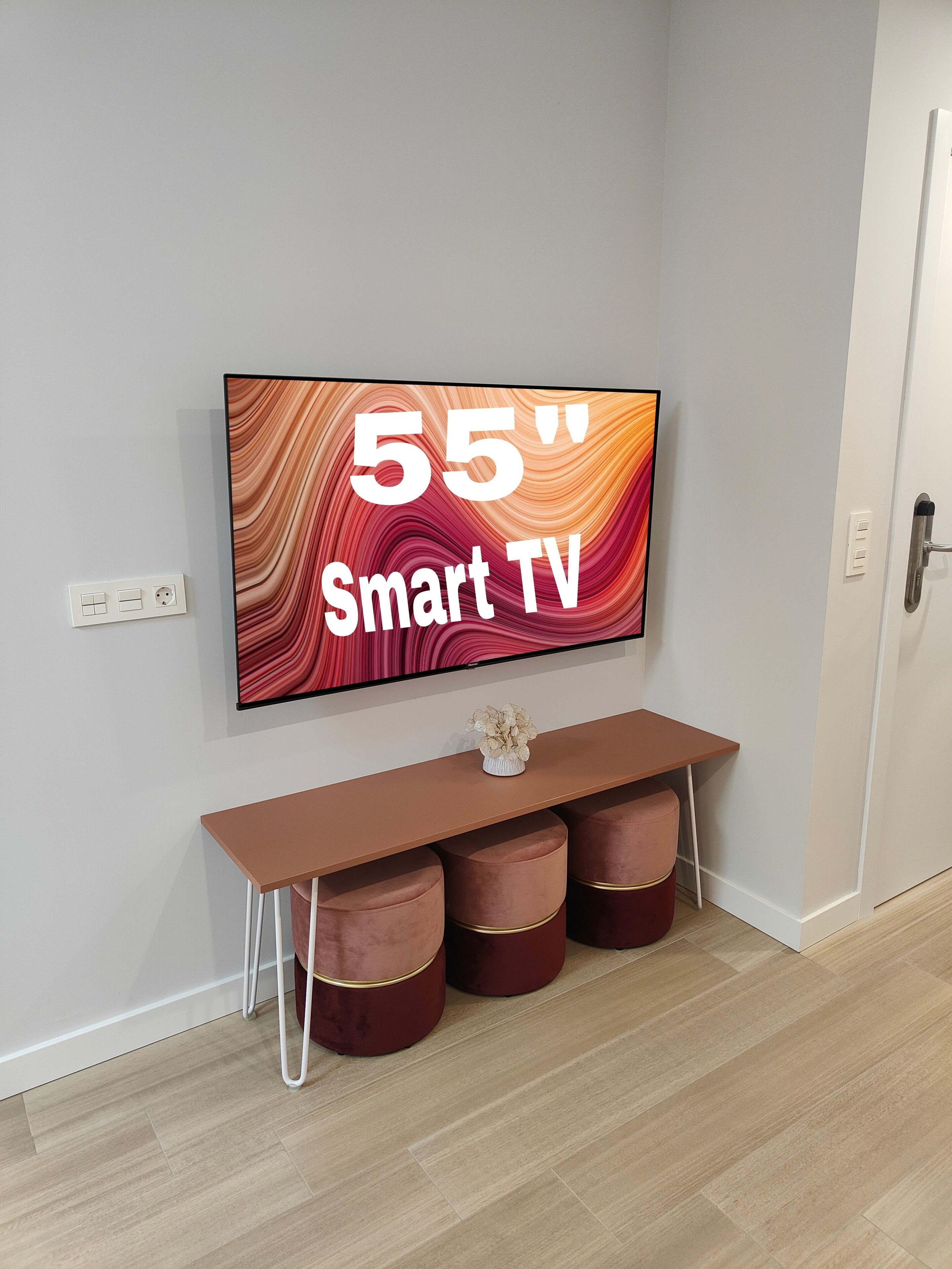 Ein 55 Zoll Smart-TV an der Wand über einem Konsolentisch mit gepolsterten Hockern.