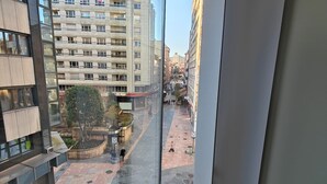 Udsigt fra en høj bygning med glasvindue, der kigger ud over et fodgængerområde med bygninger i baggrunden.