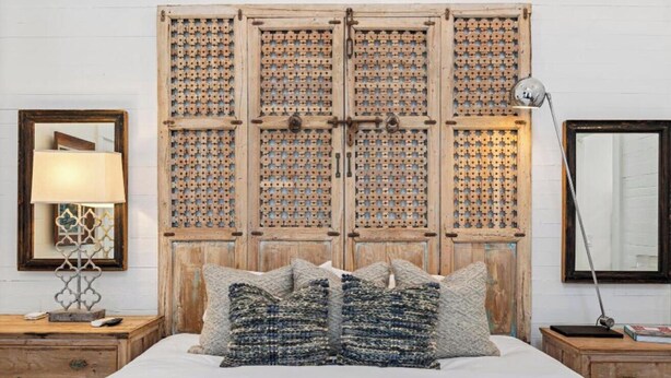 Un dormitorio con una cama grande, cabecera de madera, mesitas de noche, una lámpara y un espejo.