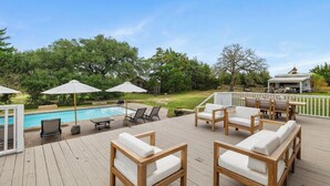 A wooden deck with outdoor furniture, a pool, and a gazebo in the background.