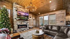 A cozy living room with a stone fireplace, a large TV, and a Christmas tree.