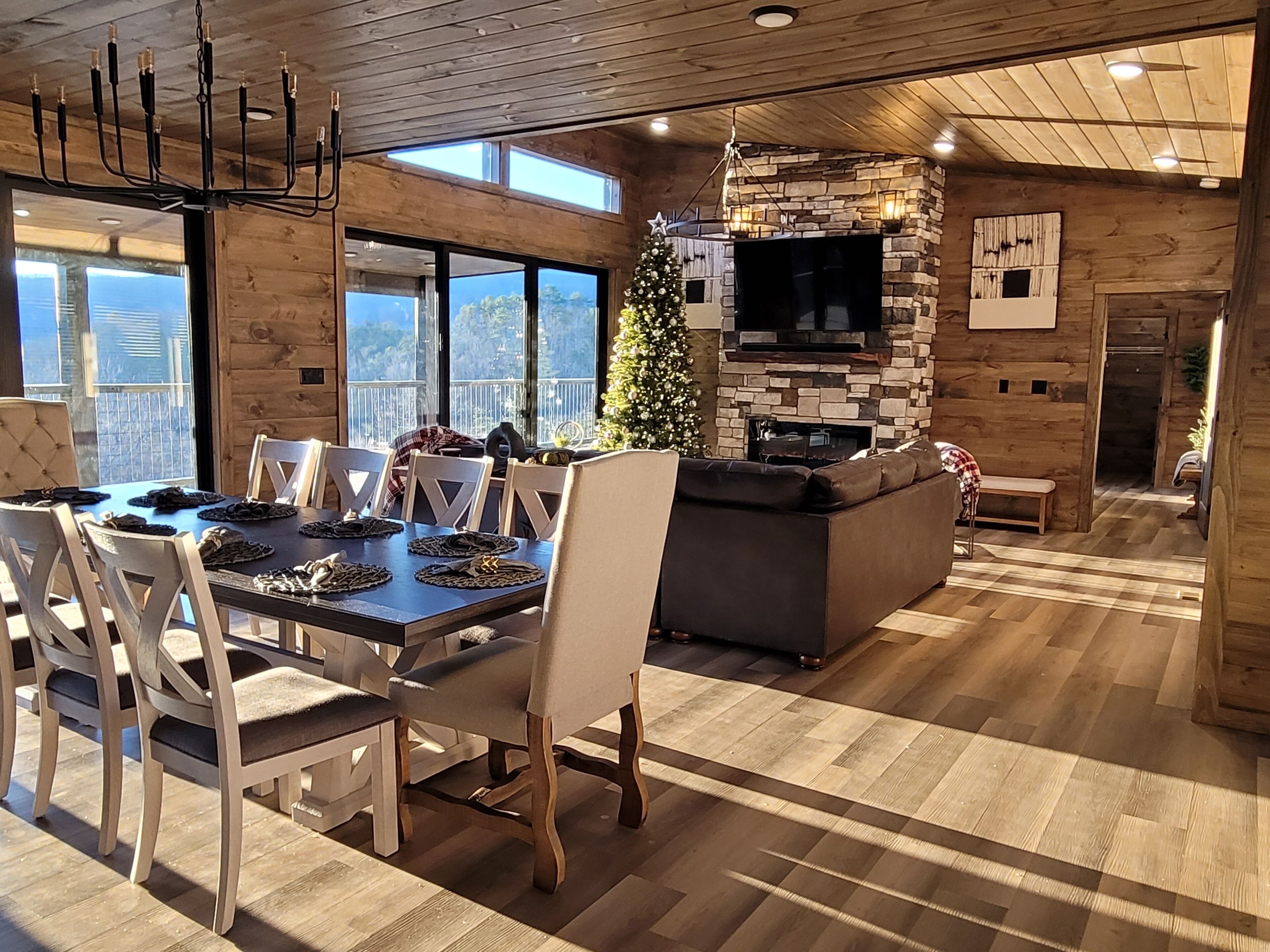 A modern dining area with a wooden table and chairs, a stone fireplace, and a Christmas tree.