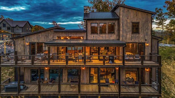 A large wooden house with multiple levels, featuring outdoor seating areas and large windows.