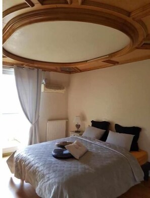 Ein Schlafzimmer mit einem Bett, einem Nachttisch, einer Lampe und einem Fenster mit Vorhängen.