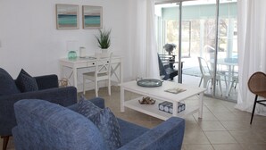 A living room with blue sofas, a white coffee table, and a dining area with a white table and chairs. There are two paintings on the wall and a plant on the coffee table. - Marco Island Pool Home: Lake and Sunset Views, 2 bedrooms, 2 bath . Pet Friendly (Marco Island)