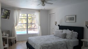 A bedroom with a bed, a ceiling fan, a window with curtains, a bedside table, and a framed picture on the wall. - Marco Island Pool Home: Lake and Sunset Views, 2 bedrooms, 2 bath . Pet Friendly (Marco Island)