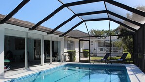 An indoor swimming pool with a glass enclosure, adjacent to a covered patio area with outdoor seating and a view of a residential neighborhood. - Marco Island Pool Home: Lake and Sunset Views, 2 bedrooms, 2 bath . Pet Friendly (Marco Island)