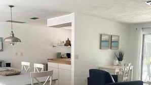 A modern kitchen with white cabinets, a dining area with a white table and chairs, and a blue armchair. - Marco Island Pool Home: Lake and Sunset Views, 2 bedrooms, 2 bath . Pet Friendly (Marco Island)