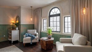A cozy living room with a large arched window, a white sofa, a wooden coffee table, and a white armchair. - Inkwell Suite at Spofford Lodge (Bucksport)
