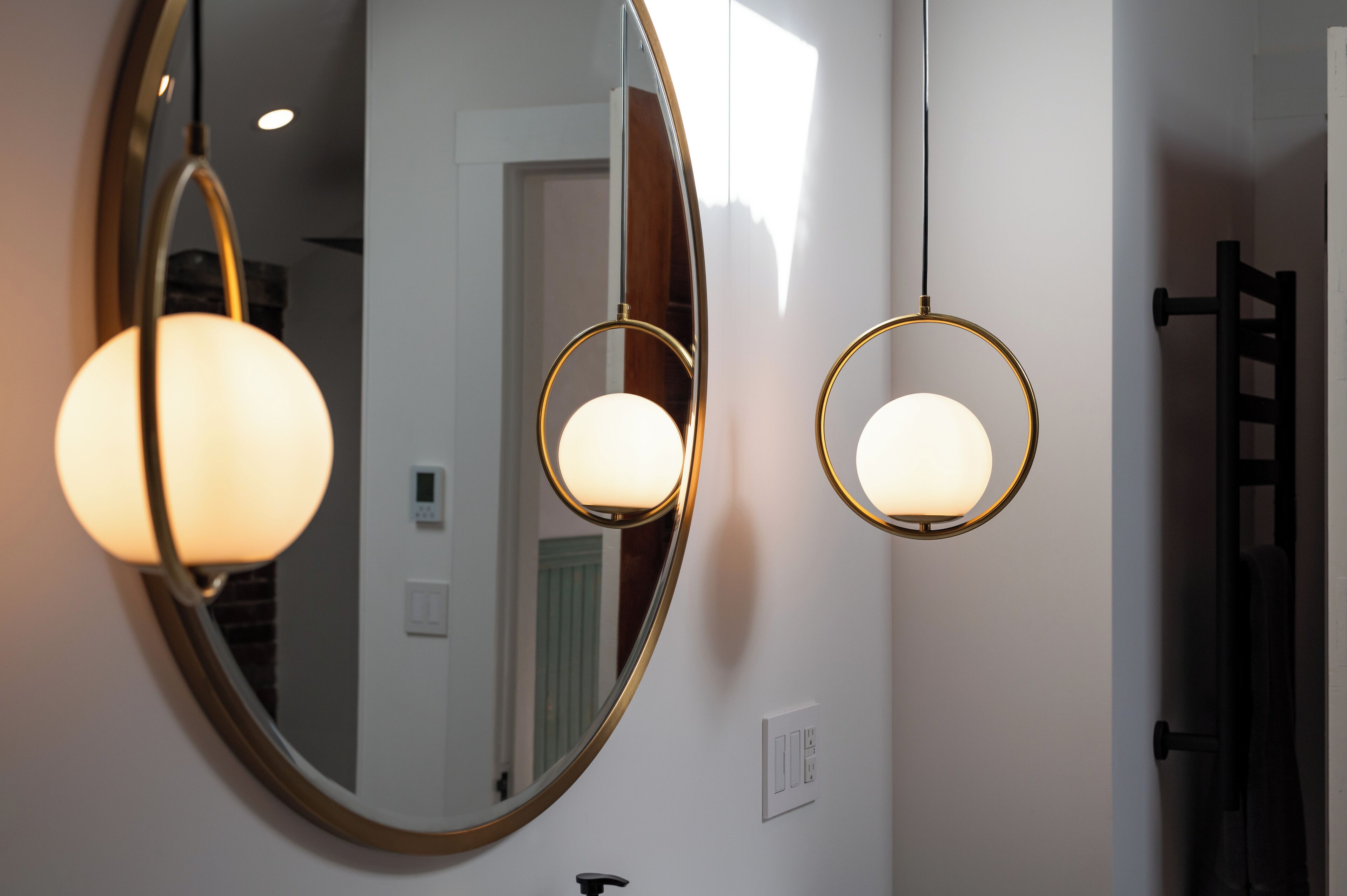 Een badkamer met een grote spiegel, twee hanglampen en een handdoekrek.