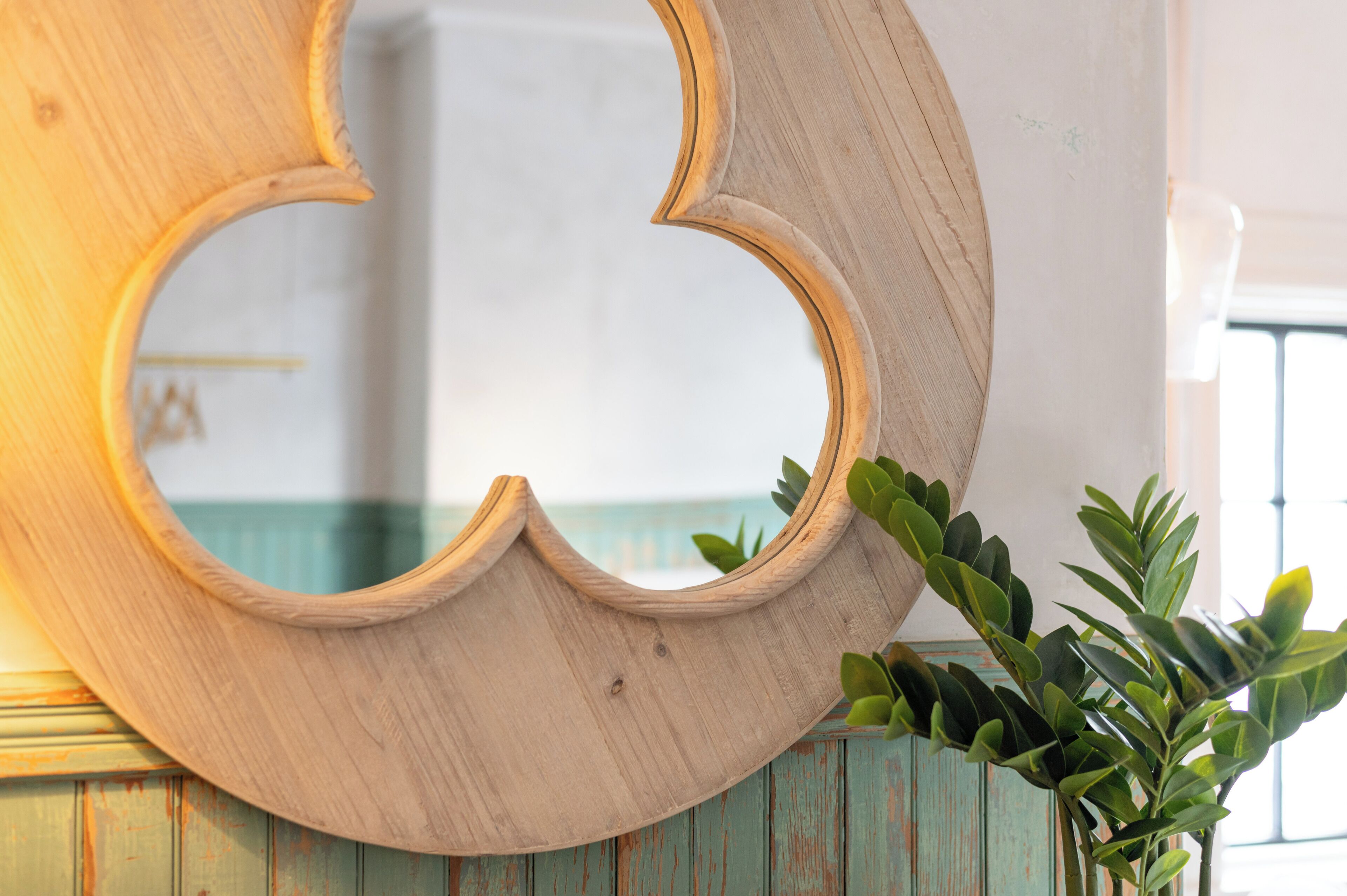 Uno specchio in legno dal design originale, appoggiato su un muro con una porta blu rustica e una pianta verde accanto.