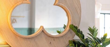 Uno specchio in legno dal design originale, appoggiato su un muro con una porta blu rustica e una pianta verde accanto.