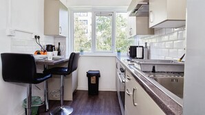 A compact kitchen with a window, a bar stool, a trash bin, and a sink. - Charming City 1-bed Apartment in Birmingham (Birmingham)