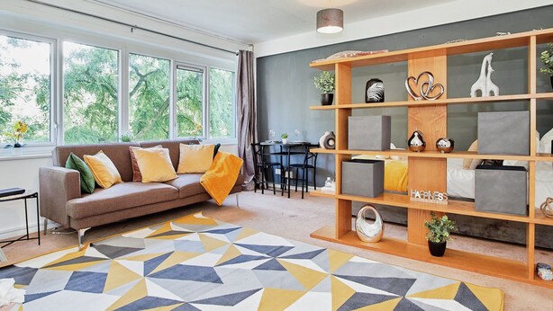 A modern living room with a sofa, a geometric patterned rug, a wooden bookshelf, and a dining area with a table and chairs. - Charming City 1-bed Apartment in Birmingham (Birmingham)