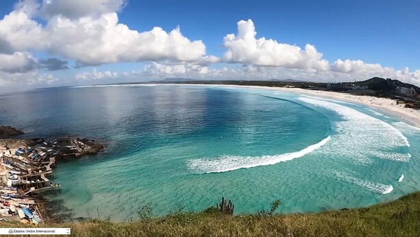 Un paysage côtier avec une eau turquoise et limpide, une plage de sable et une zone rocheuse où se trouvent des bateaux.
