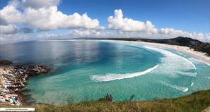 Een kustlandschap met helder turquoise water, een zandstrand en een rotsachtig gebied met boten.