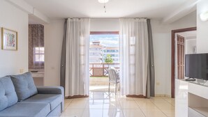Un salon moderne avec un canapé, un téléviseur et un balcon offrant une vue sur les immeubles.