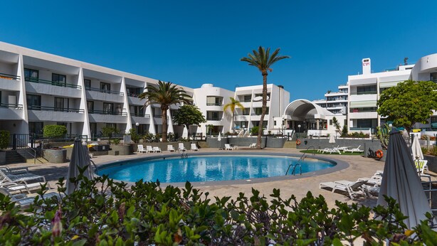 A pool area with lounge chairs and palm trees, surrounded by modern buildings. - GO2TENERIFE Apart'Jara Pool view & Beach at 5 min (Playa de las Americas)