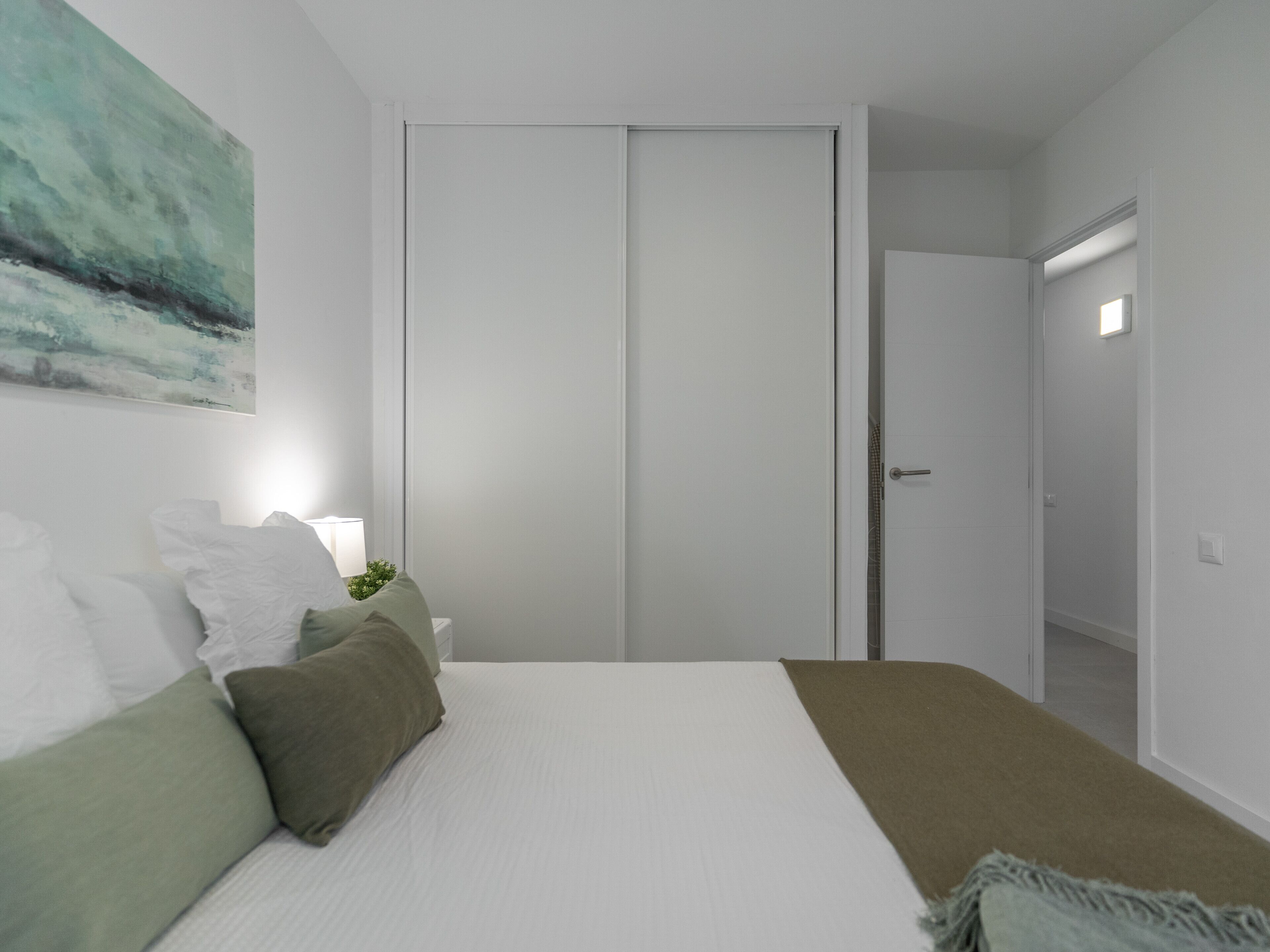 Een slaapkamer met een bed, kussens, een nachtkastje, een schilderij en een inloopkast.