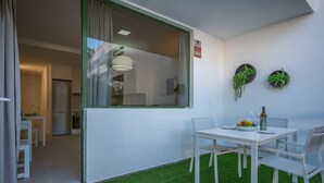 A modern kitchen with a built-in fridge, a dining area with a white table and chairs, and a small balcony with artificial grass. - GO2TENERIFE Apart'Jara Pool view & Beach at 5 min (Playa de las Americas)