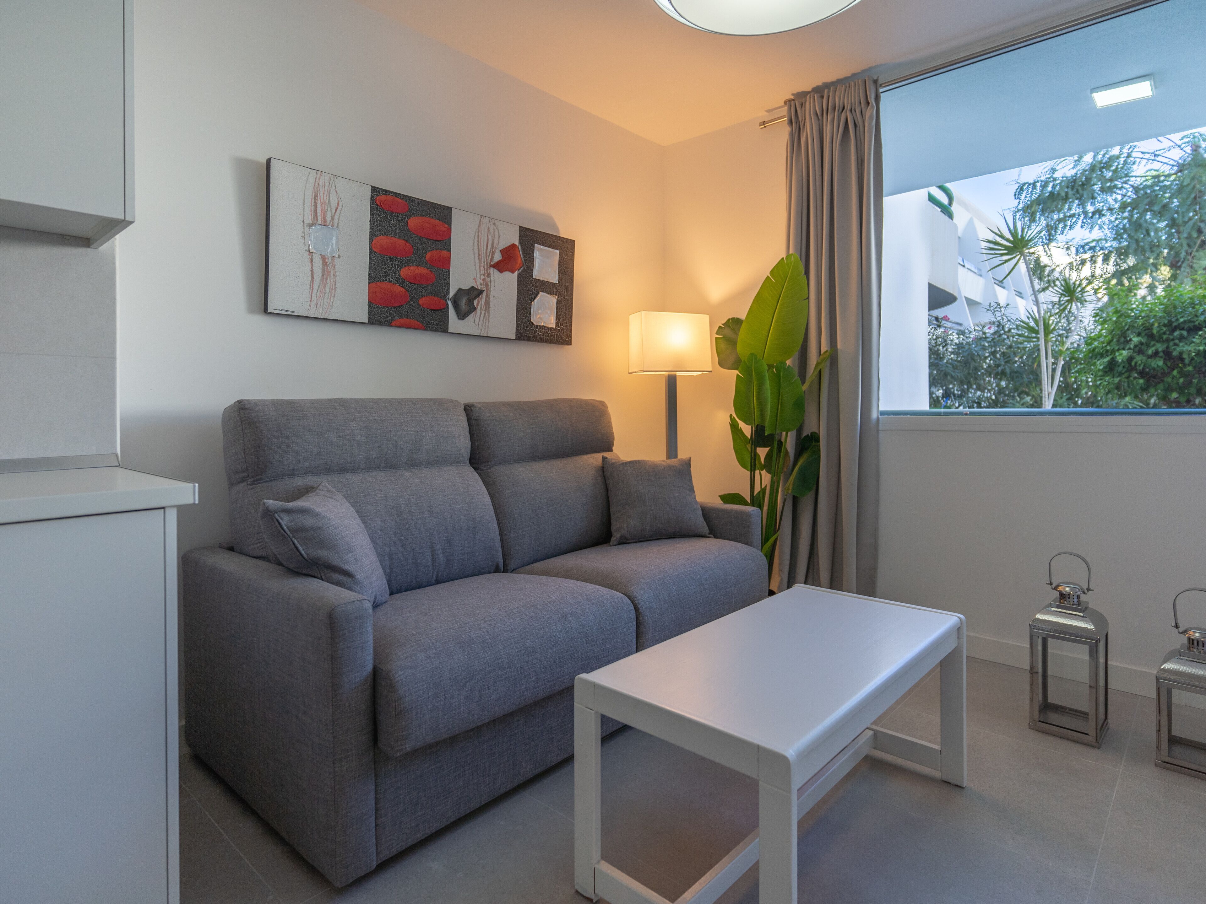 Uma sala de estar moderna com um sofá cinzento, uma mesa de centro branca e um abajur.