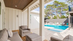 Un espace extérieur abrité, doté d’une piscine, de meubles en osier et offrant une vue sur les arbres.