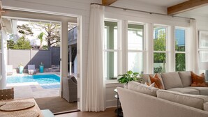 Un salon moderne avec un canapé beige, une table basse en bois et une vue sur une piscine et un espace de détente extérieur.