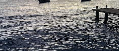 A calm sea with several boats anchored near a pier.