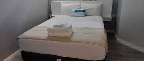 Un dormitorio pequeño y funcional con una cama individual, una mesita de noche, una ventana y un aire acondicionado de pared.