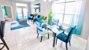 Een ruime eethoek met een glazen tafel, blauwe fauteuils en een plafondventilator.