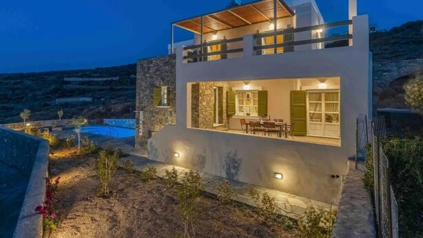 Ein modernes, zweistöckiges Haus mit Natursteinfassade, einem Balkon und einem Pool im Hintergrund.