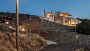 A modern house with stone walls and a flat roof, surrounded by dry grass and a stone wall. - Stelios-Korina Villa with Pool an Stunning View Posidonia Syros Cyclades Greece
 (Posidonia, Syros)