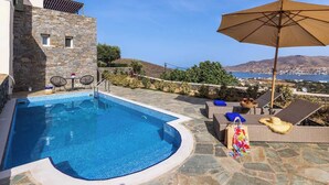 Ein Swimmingpool mit Steinmauern, Liegestühlen und Blick auf das Meer.