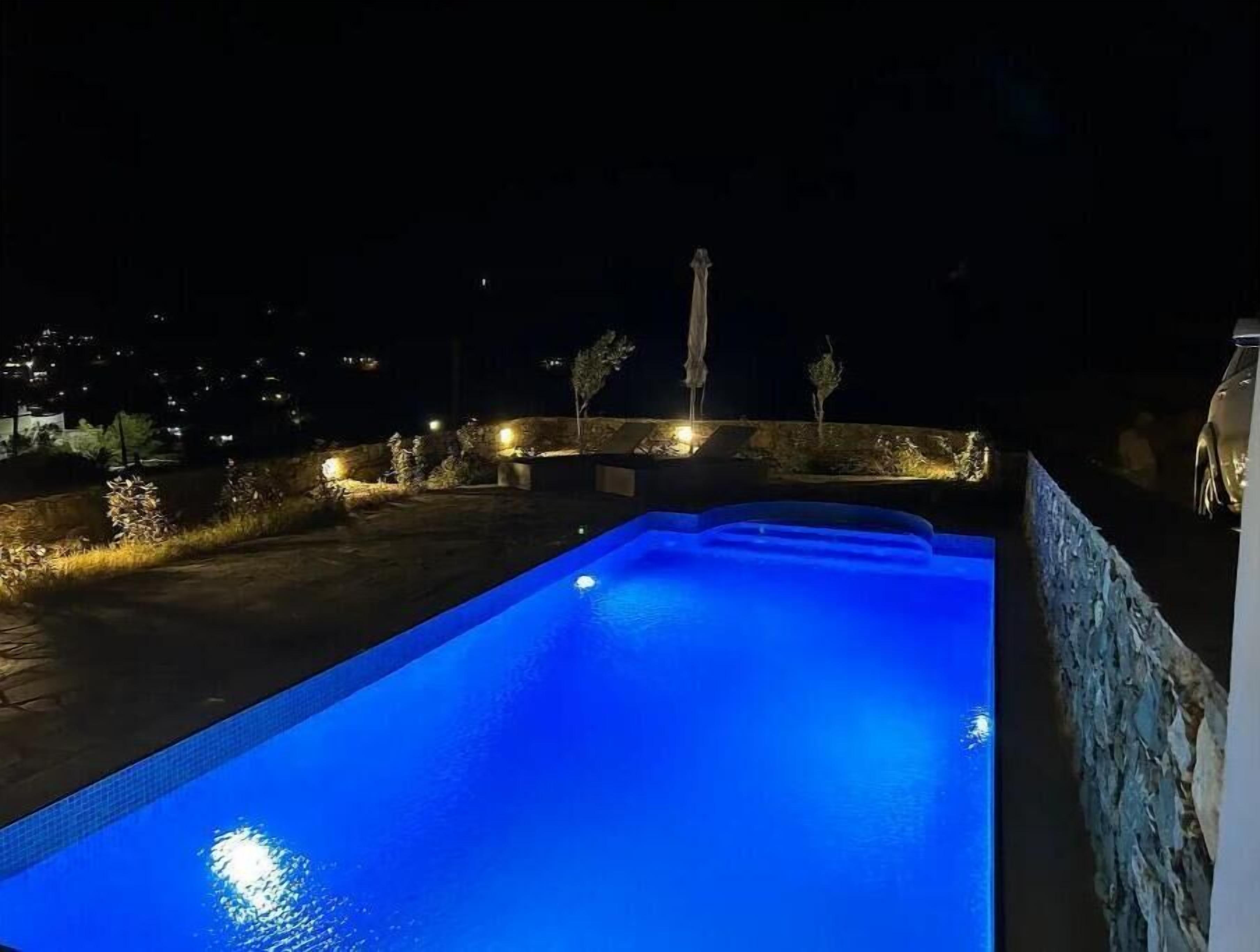 Una piscina de nit amb llums al voltant i una vista llunyana d'un paisatge urbà.