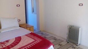 A bedroom with a bed, a wooden nightstand, a radiator, and a door with a mirror. - Double Room with Mountain View - Sheikh Mousa Bedouin camp

 (محافظة الوادي الجديد)