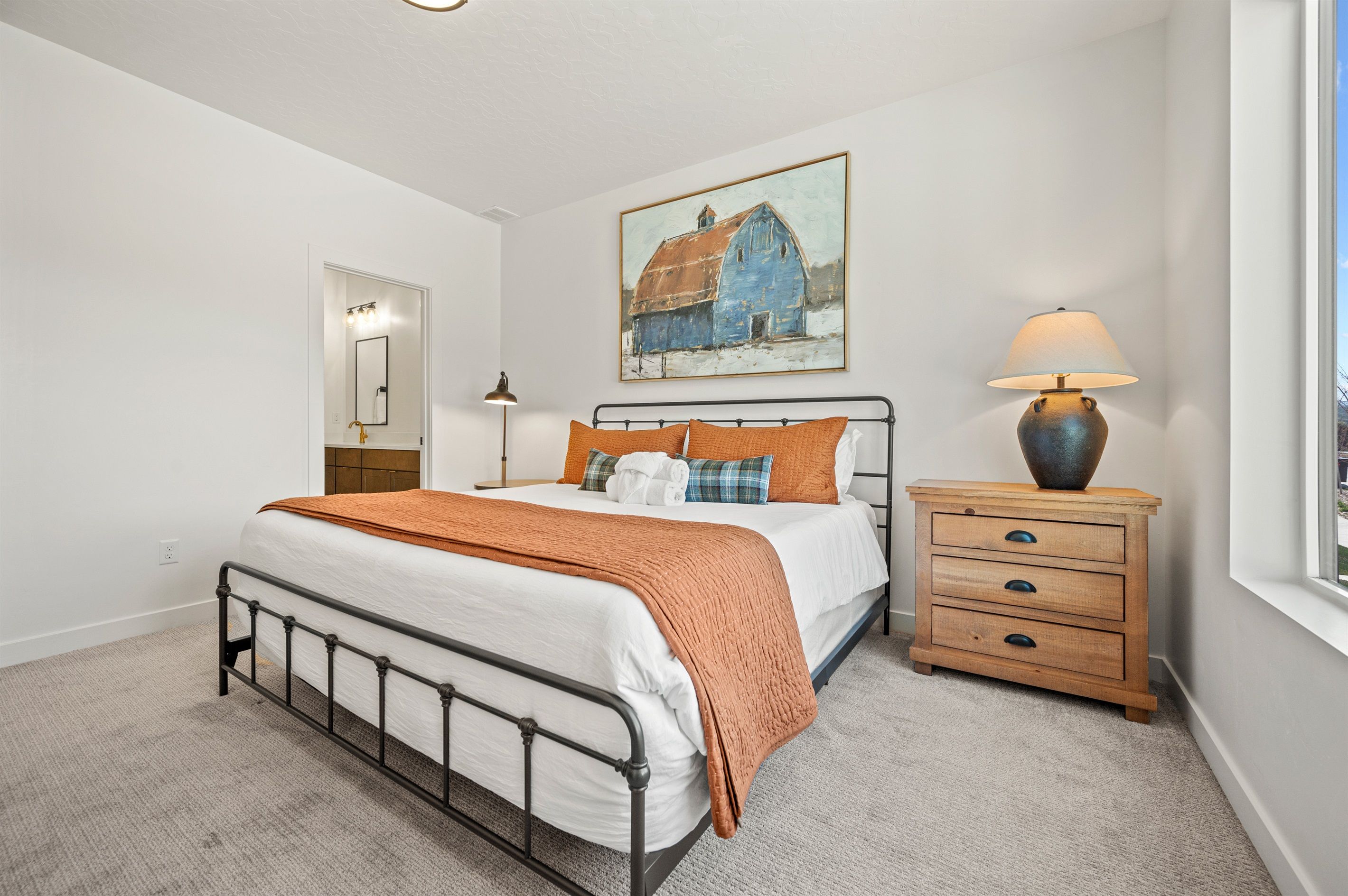 A bedroom with a bed, bedside table, lamp, and a painting on the wall.