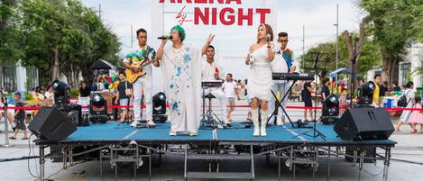 Un escenario con una banda tocando en un evento al aire libre, con un cartel que dice "ARENA NIGHT".