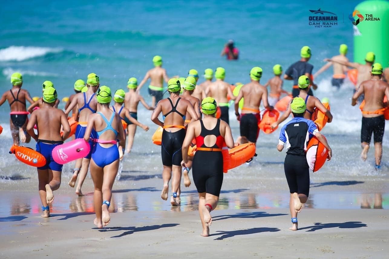 A group of people running on a beach, some carrying life vests.