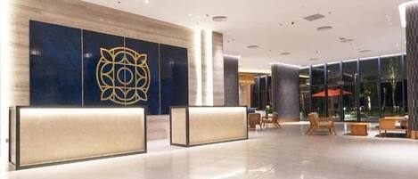 A modern lobby with a reception desk, seating area, and large windows.