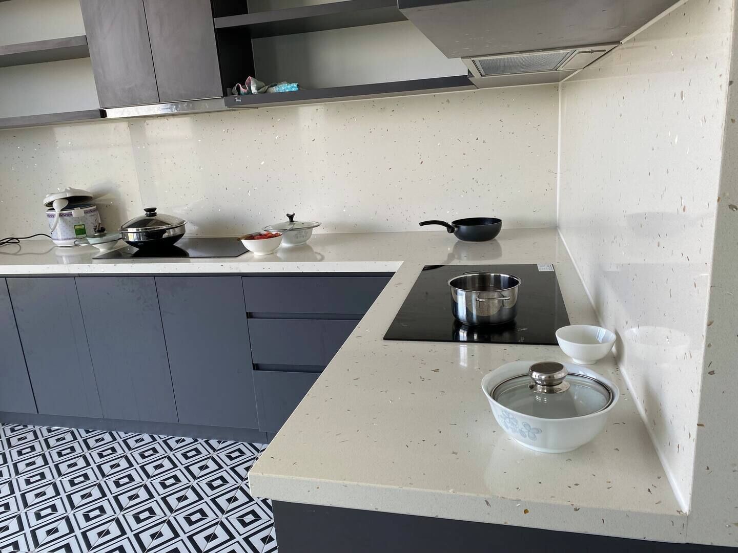 A modern kitchen with a white countertop, grey cabinets, and a patterned floor.