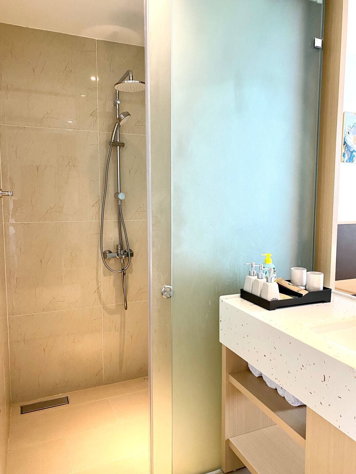 Un baño moderno con cabina de ducha de vidrio, un lavamanos blanco con artículos de aseo y un mueble de tocador de madera.