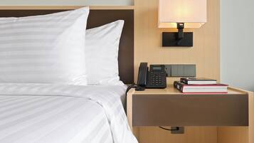 A neatly made bed with white bedding, a bedside table with a telephone, a lamp, and a few books.