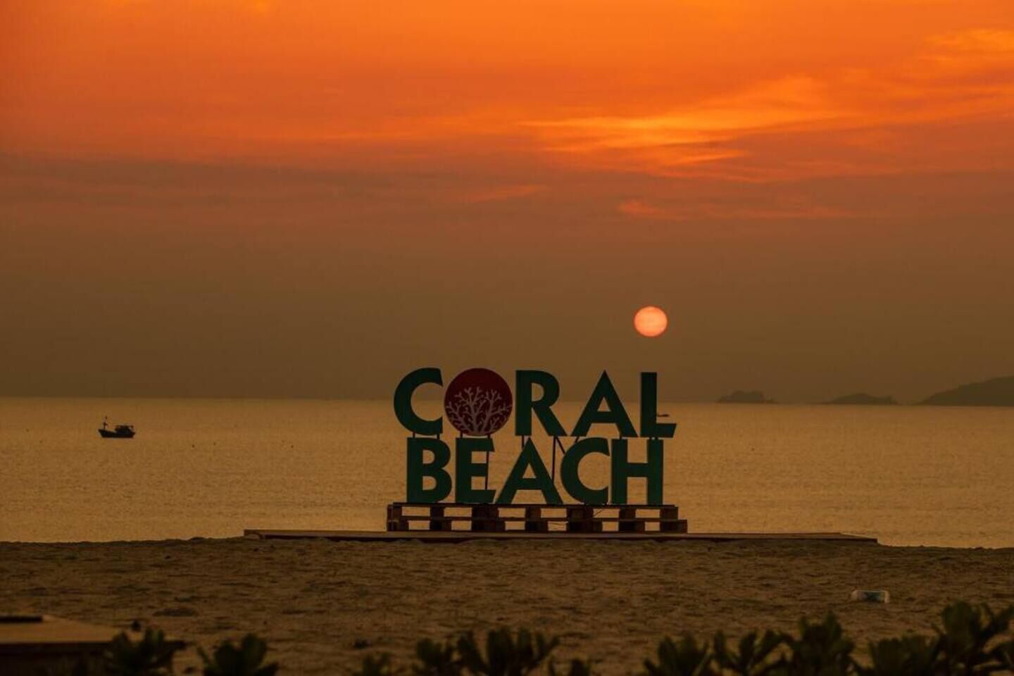 A sign with "CORAL BEACH" and a tree logo, set against a sunset over water.