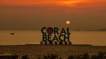 A sign with "CORAL BEACH" and a tree logo, set against a sunset over water.
