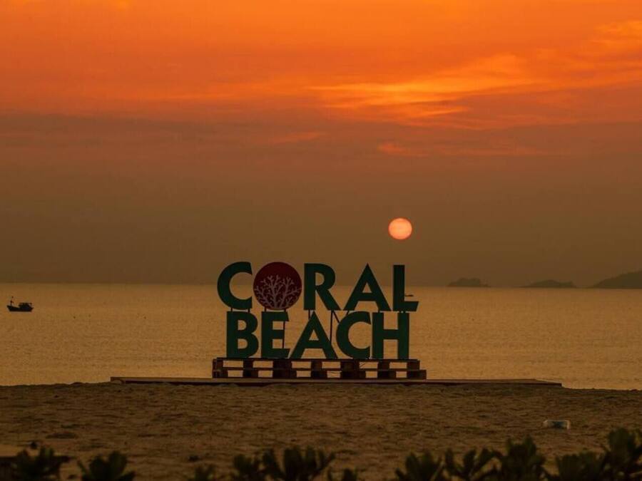 A sign with "CORAL BEACH" and a tree logo, set against a sunset over water.