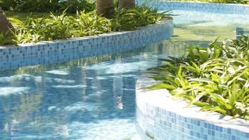 Ein Pool mit blauen Mosaikfliesen, umgeben von üppiger Vegetation und Palmen.