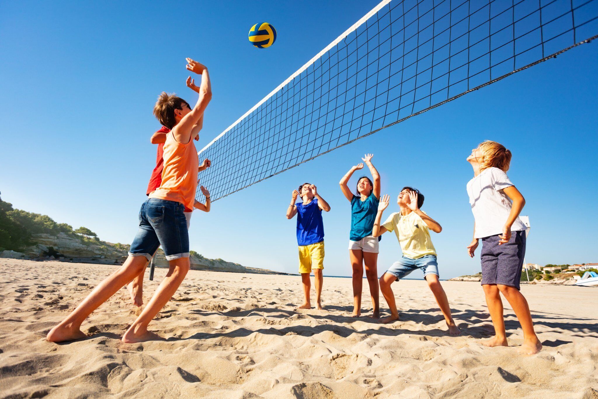 Eine Gruppe Menschen spielt Beachvolleyball auf sandigem Strand bei blauem Himmel.