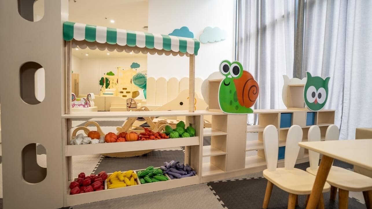 Ein Kinderspielbereich mit einem kleinen Laden, Regalen voller Spielzeug und verschiedenen bunten Artikeln sowie zwei eulenähnlichen Dekorationen.