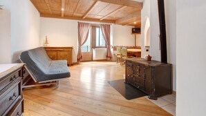 A room with a wooden ceiling, a reclining chair, a wooden cabinet, and a window with curtains. - Apartment 'Premesan 5' with Wi-Fi (Bormio)